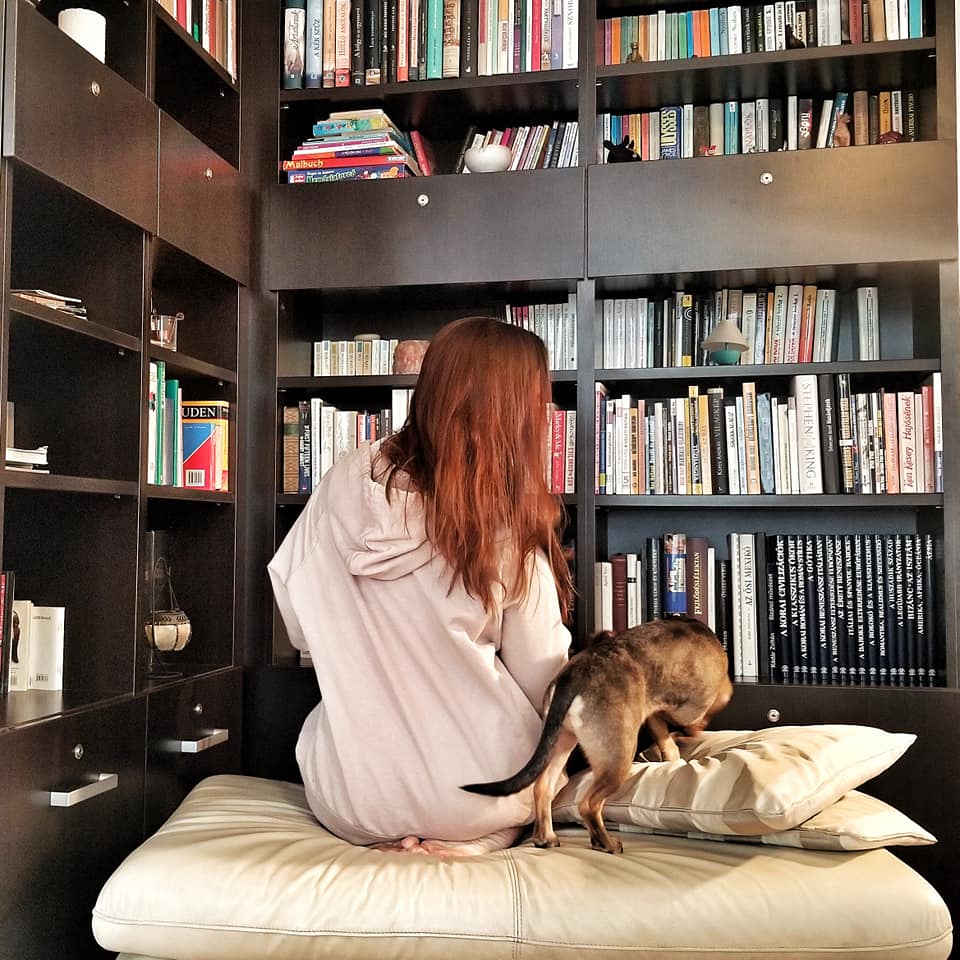 Woman and dog sitting in front of huge bookshelves facing away from camera.